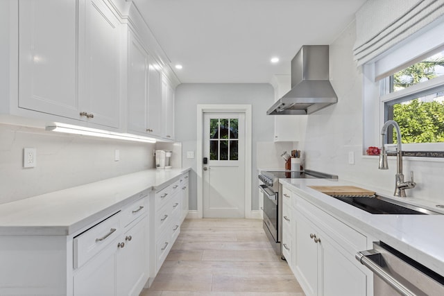 kitchen with white cabinetry, sink, wall chimney range hood, light hardwood / wood-style floors, and appliances with stainless steel finishes