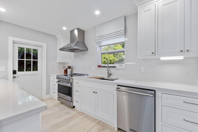 kitchen with light hardwood / wood-style flooring, wall chimney exhaust hood, white cabinets, and appliances with stainless steel finishes