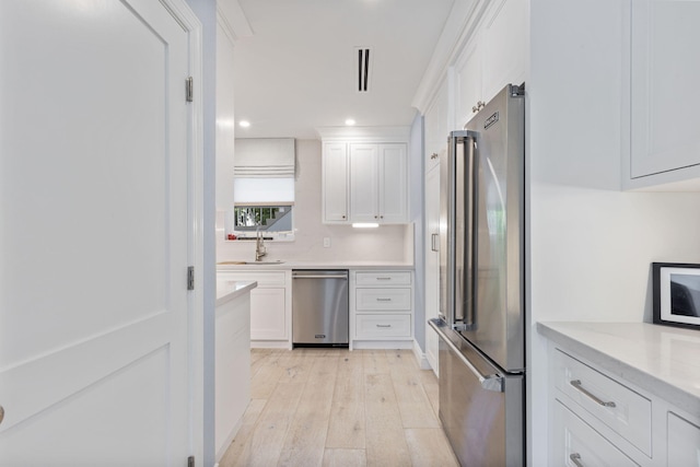 kitchen with white cabinetry, light wood-type flooring, stainless steel appliances, and light stone counters