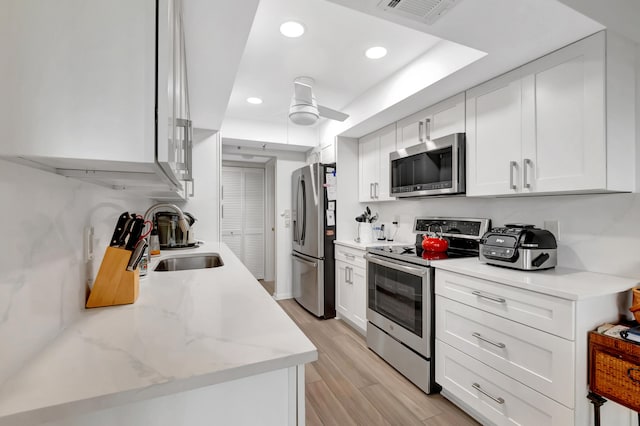 kitchen with light stone countertops, sink, light hardwood / wood-style flooring, white cabinets, and appliances with stainless steel finishes