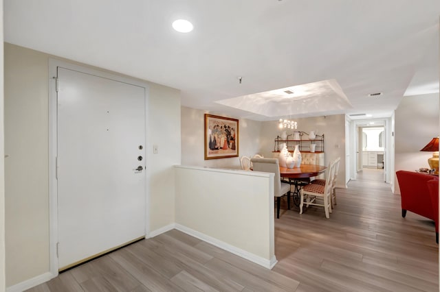 foyer entrance featuring light hardwood / wood-style floors, a tray ceiling, and a notable chandelier