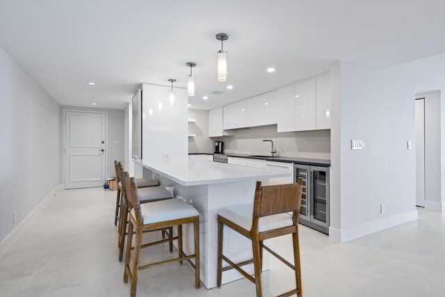kitchen featuring tasteful backsplash, beverage cooler, sink, white cabinetry, and hanging light fixtures
