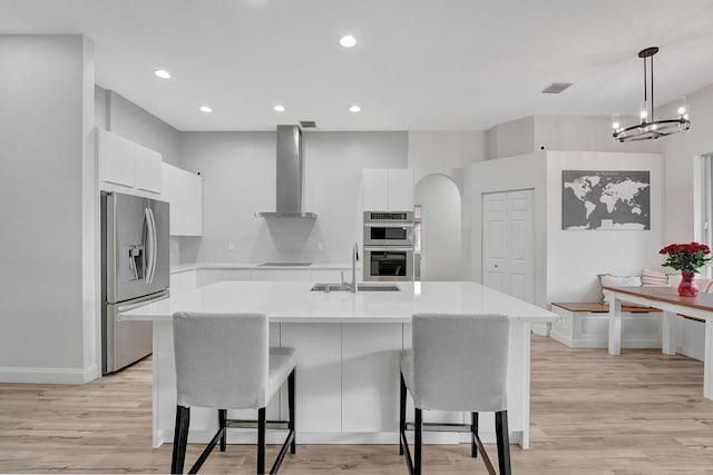 kitchen featuring white cabinets, light wood-type flooring, stainless steel appliances, and wall chimney range hood