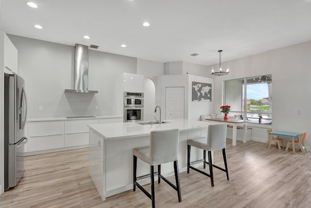 kitchen with white cabinets, appliances with stainless steel finishes, sink, and wall chimney range hood