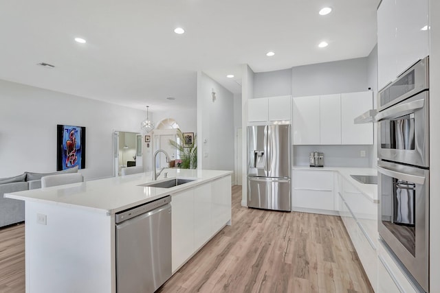 kitchen with light hardwood / wood-style floors, sink, appliances with stainless steel finishes, an island with sink, and white cabinets