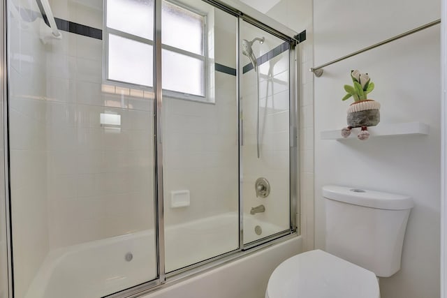 bathroom featuring toilet and shower / bath combination with glass door