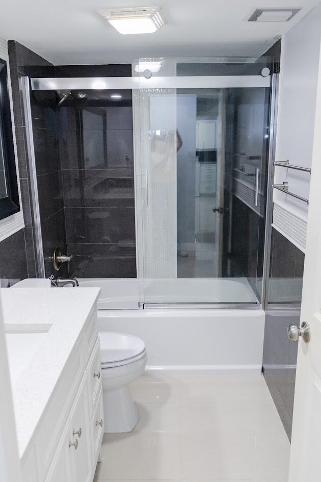 full bathroom with tile patterned flooring, shower / bath combination with glass door, toilet, and vanity