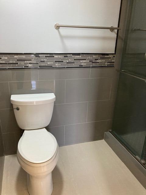 bathroom with tile walls, an enclosed shower, and toilet