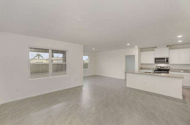 kitchen featuring sink, an island with sink, light stone countertops, white cabinetry, and appliances with stainless steel finishes