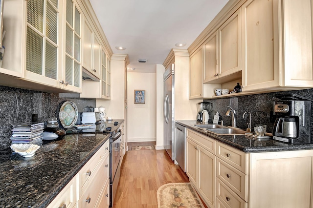 kitchen featuring dark stone counters, sink, tasteful backsplash, light hardwood / wood-style floors, and stainless steel appliances