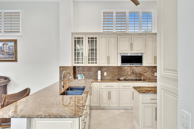 kitchen with backsplash, black electric stovetop, sink, light stone countertops, and a breakfast bar area