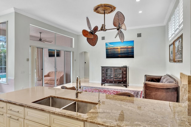 kitchen featuring cream cabinets, sink, ornamental molding, light stone countertops, and decorative light fixtures