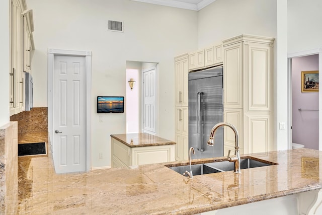 kitchen with cream cabinets, sink, crown molding, light stone countertops, and stainless steel built in refrigerator