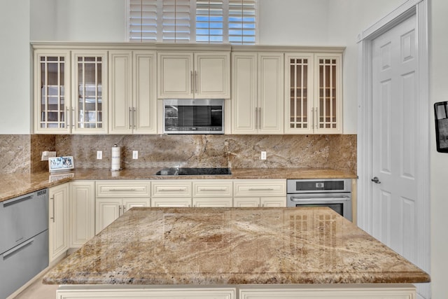 kitchen featuring tasteful backsplash, light stone countertops, stainless steel appliances, and cream cabinets