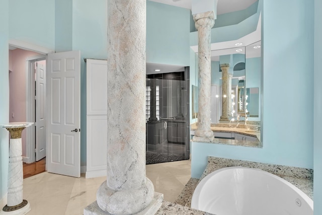 bathroom featuring a towering ceiling, a tub, and decorative columns