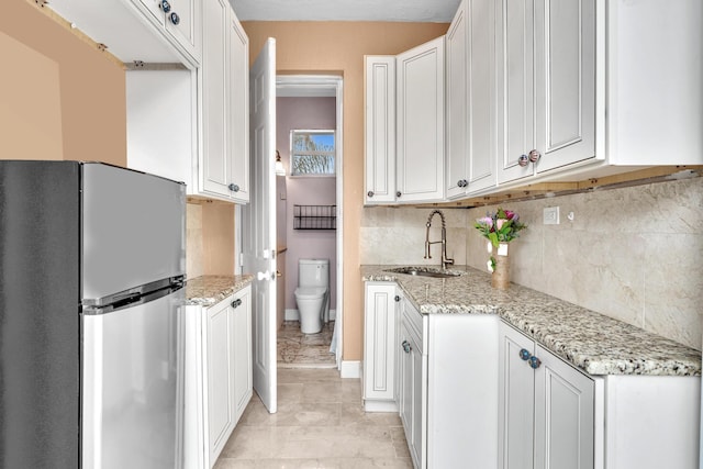 kitchen featuring decorative backsplash, stainless steel fridge, light stone countertops, sink, and white cabinets