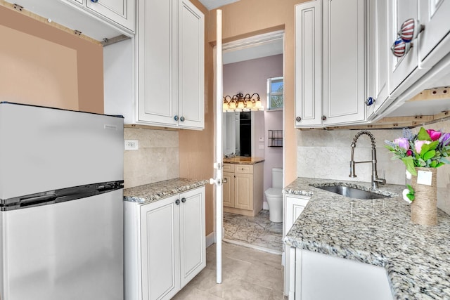 kitchen featuring sink, decorative backsplash, stainless steel fridge, light stone countertops, and white cabinetry