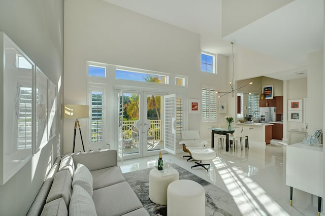 living room featuring a chandelier, french doors, a towering ceiling, and plenty of natural light