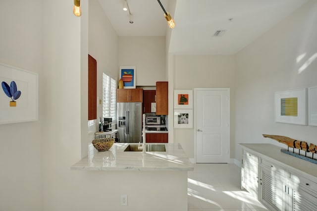 kitchen featuring sink, kitchen peninsula, light tile patterned floors, a towering ceiling, and stainless steel fridge with ice dispenser