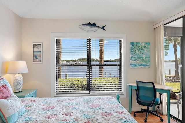 bedroom with a textured ceiling, a water view, and hardwood / wood-style flooring