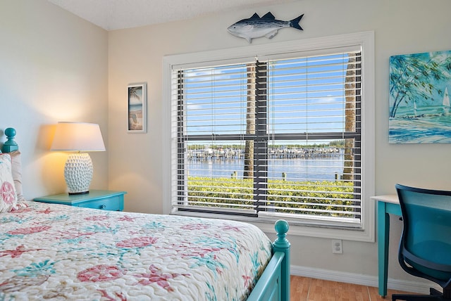 bedroom with light hardwood / wood-style floors, a water view, and a textured ceiling