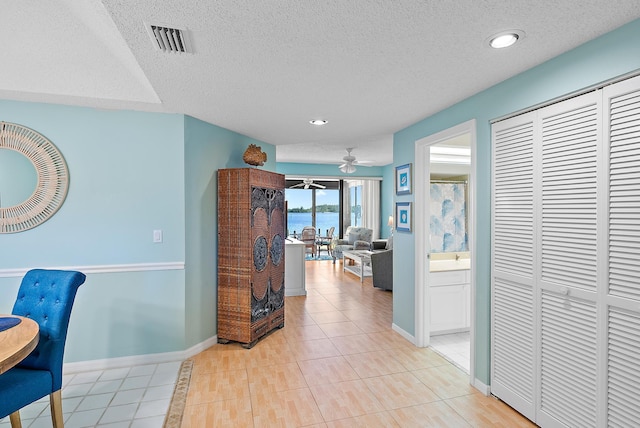 corridor with light tile patterned flooring, a water view, and a textured ceiling