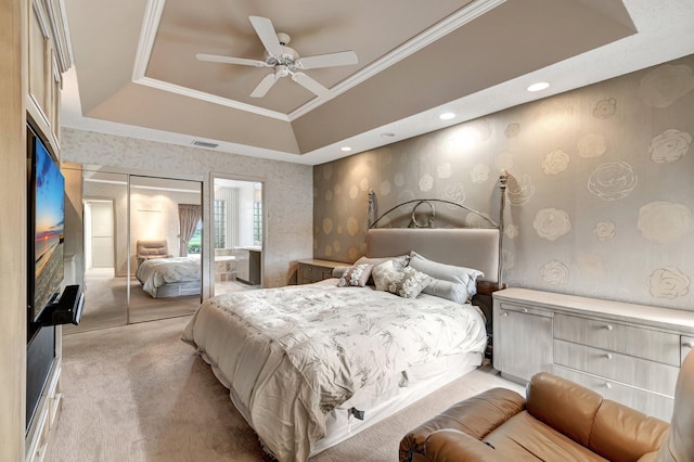 carpeted bedroom with ceiling fan, crown molding, a tray ceiling, and a closet