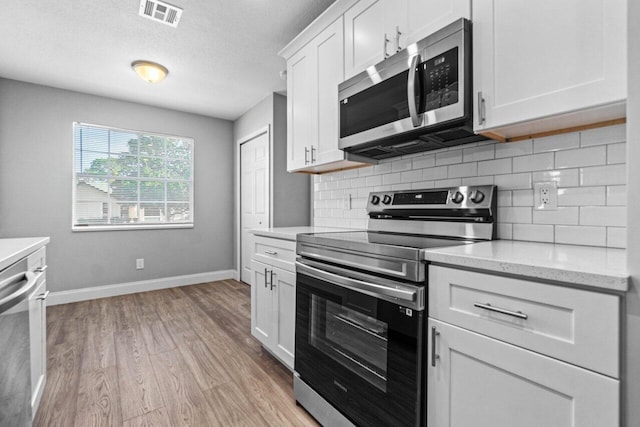 kitchen featuring light stone countertops, backsplash, stainless steel appliances, white cabinets, and light hardwood / wood-style floors