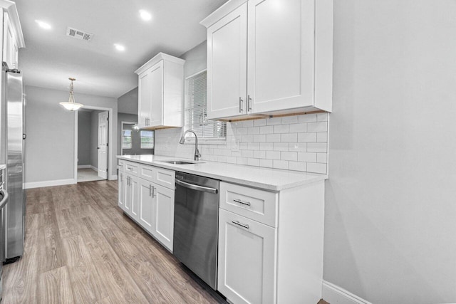 kitchen featuring appliances with stainless steel finishes, light wood-type flooring, sink, decorative light fixtures, and white cabinets