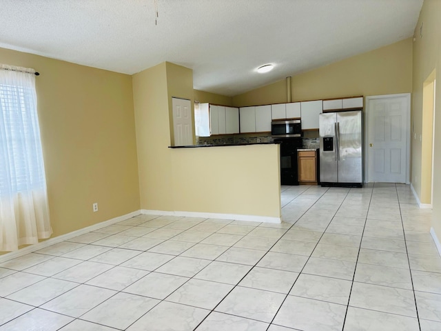 kitchen with light tile patterned flooring, vaulted ceiling, decorative backsplash, white cabinets, and appliances with stainless steel finishes