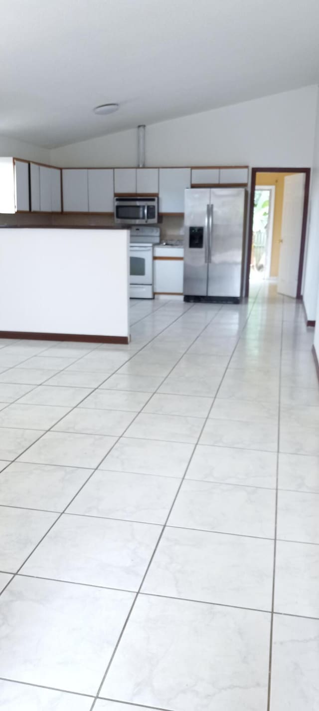 kitchen with appliances with stainless steel finishes, light tile patterned floors, and vaulted ceiling