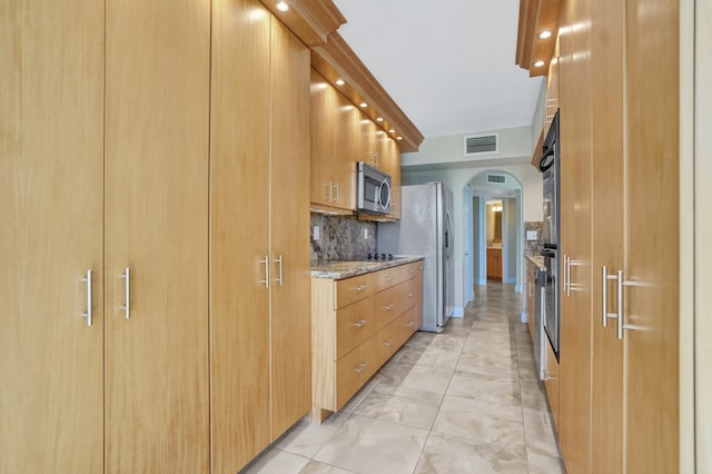 kitchen featuring light tile patterned floors, light stone countertops, appliances with stainless steel finishes, and tasteful backsplash