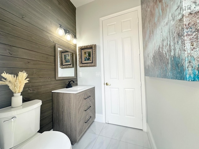 bathroom featuring vanity, wooden walls, and toilet