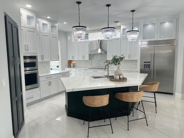 kitchen with light stone counters, a center island with sink, appliances with stainless steel finishes, sink, and wall chimney exhaust hood