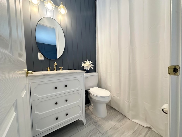 bathroom with vanity, wooden walls, and toilet