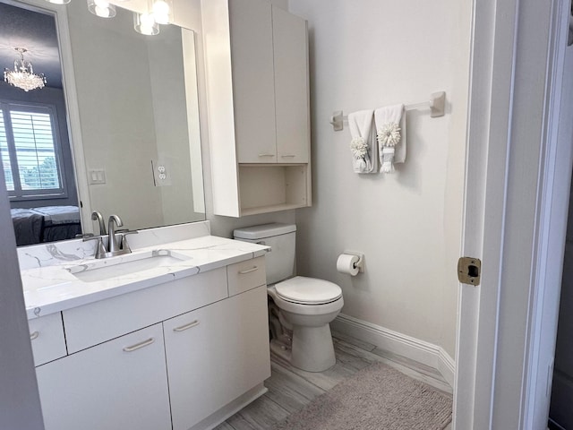 bathroom with a notable chandelier, toilet, vanity, and wood-type flooring