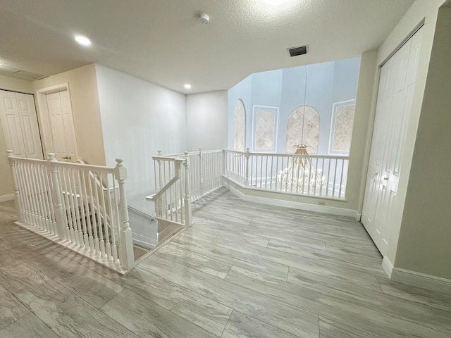 hall with light wood-type flooring and a textured ceiling