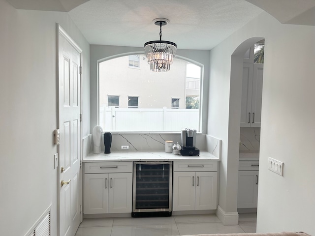 bar with decorative backsplash, hanging light fixtures, a textured ceiling, and beverage cooler