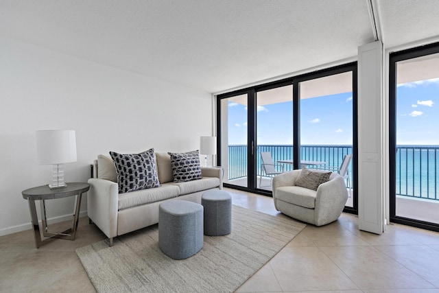 living area with light tile patterned floors, a textured ceiling, a water view, baseboards, and expansive windows