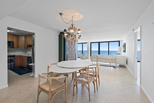 dining area featuring a chandelier, light tile patterned flooring, a water view, baseboards, and expansive windows