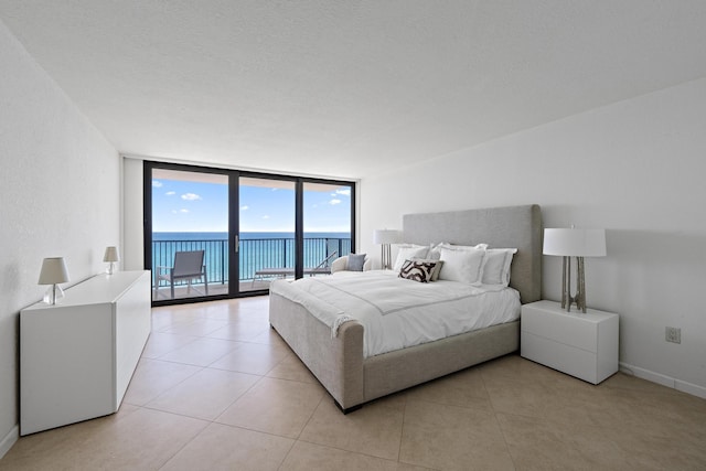 bedroom featuring light tile patterned floors, a water view, baseboards, access to exterior, and floor to ceiling windows