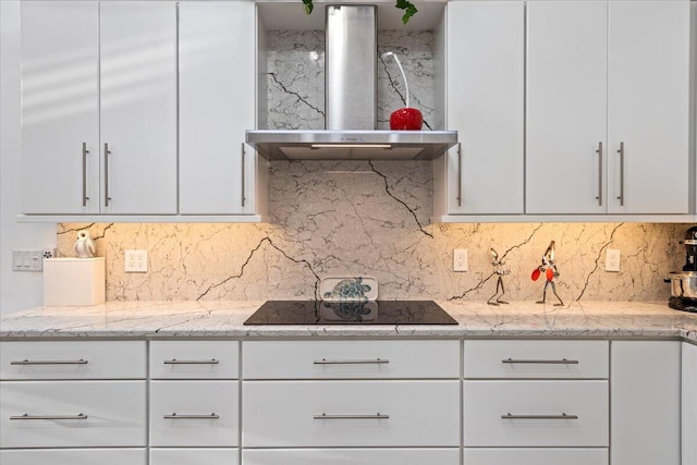 kitchen with black electric stovetop, wall chimney exhaust hood, decorative backsplash, light stone counters, and white cabinetry