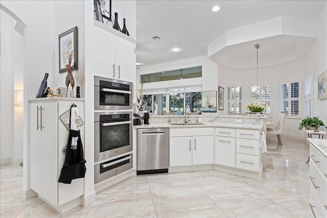 kitchen with white cabinets, hanging light fixtures, sink, light stone countertops, and appliances with stainless steel finishes