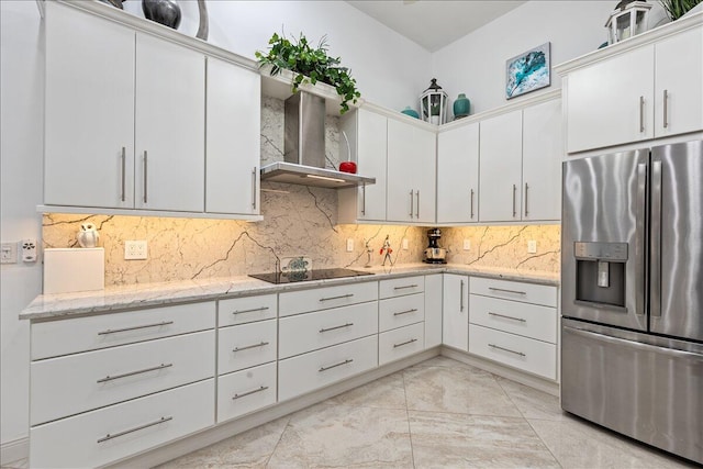 kitchen featuring white cabinetry, light stone countertops, wall chimney exhaust hood, stainless steel fridge, and decorative backsplash