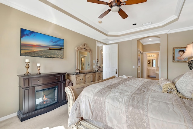 carpeted bedroom featuring a tray ceiling, connected bathroom, ceiling fan, and ornamental molding