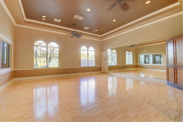 empty room with light wood-type flooring, a raised ceiling, ceiling fan, crown molding, and a high ceiling