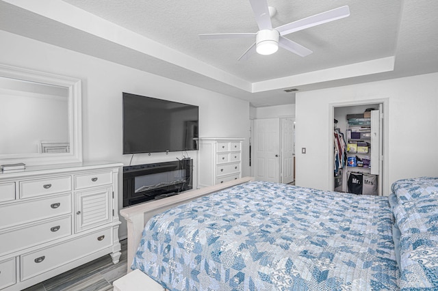 bedroom with a textured ceiling, ceiling fan, a walk in closet, and a raised ceiling