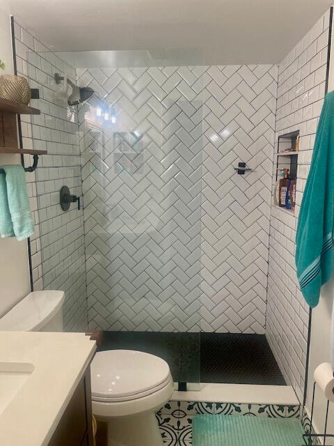 bathroom with tiled shower, tile patterned floors, vanity, and toilet