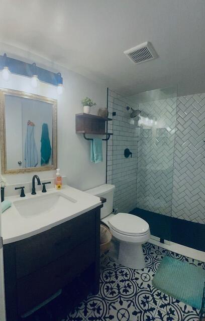 bathroom with a tile shower, tile patterned flooring, vanity, and toilet