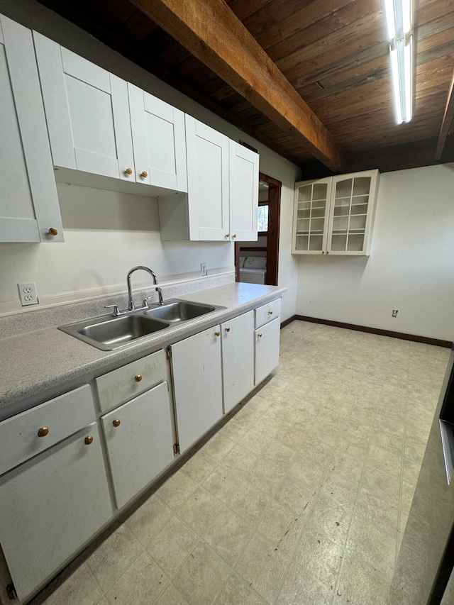 kitchen with wooden ceiling, beamed ceiling, white cabinetry, and sink